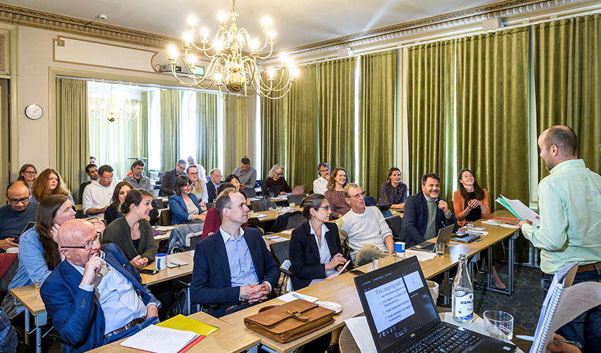 People seated in rows in a room with green curtains.