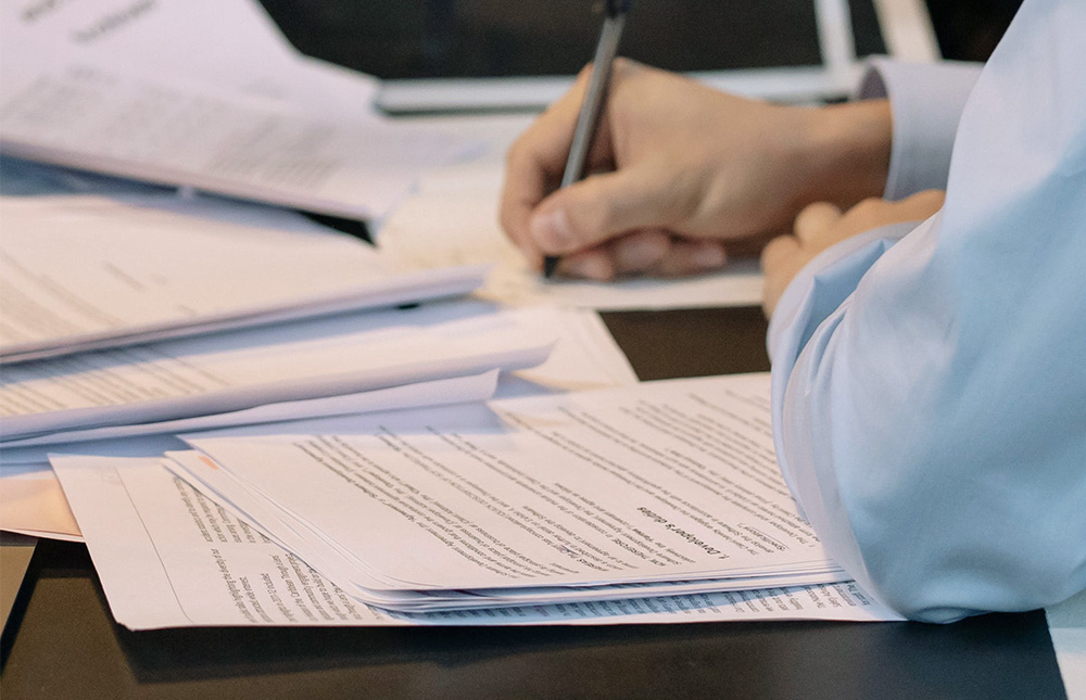 close-up of a person writing among many papers on a desk. Photo. 