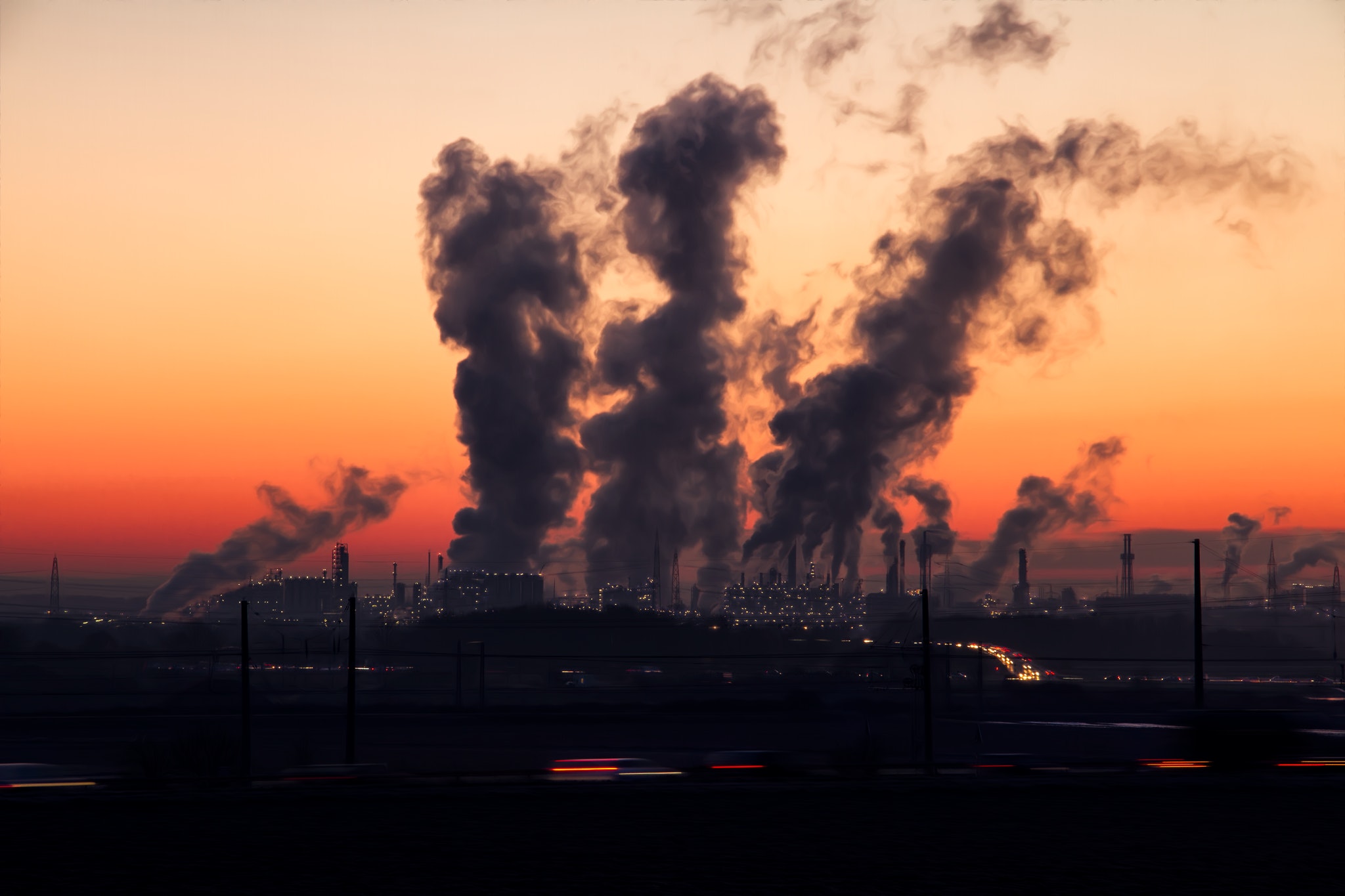 Smoke pillars from chimneys in a city. Orange sunset sky as backdrop.